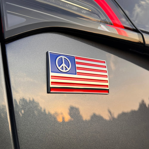 Chrome-plated peace symbol layered over an American flag design on car. Made from durable ABS plastic with a weather-resistant finish. Features strong 3M automotive-grade adhesive for secure, long-term application. Suitable for car windows, coolers, laptops, or other gear.